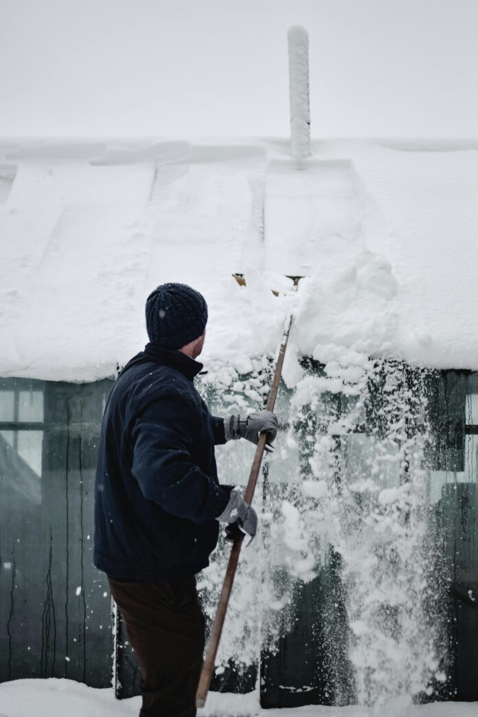homeowner inspecting a snow-covered roof, clearing debris, and sealing gutters to prepare for winter weather.